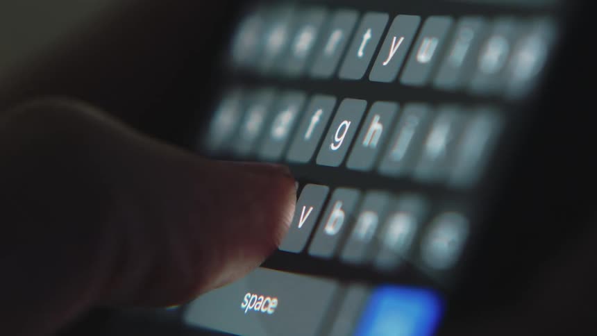 Letters glow on a small keyboard as fingers press the keys as they type on an electronic device
