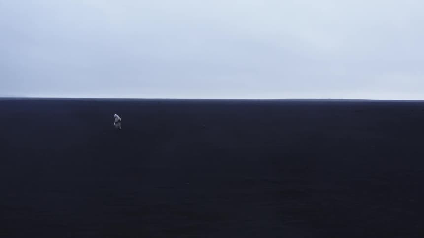 Lone person in white clothes stands in a vast dark landscape under a cloudy sky