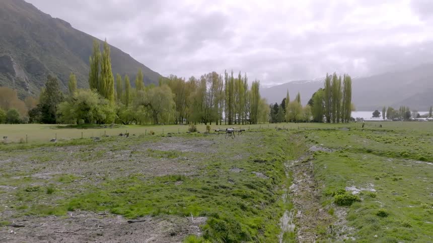 A spray drone flying over a muddy grass field
