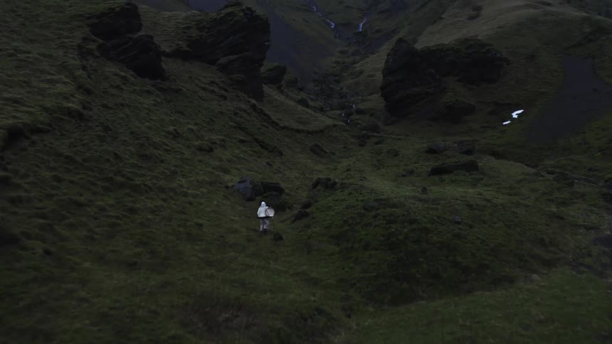 Person walking through mountainous terrain with rock formations covered in dark green vegetation