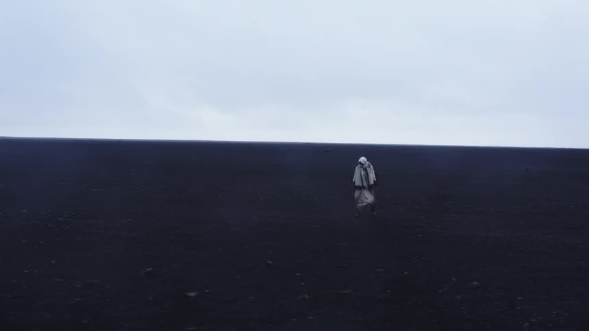 Lone person in a white spacesuit is standing in a vast dark terrain