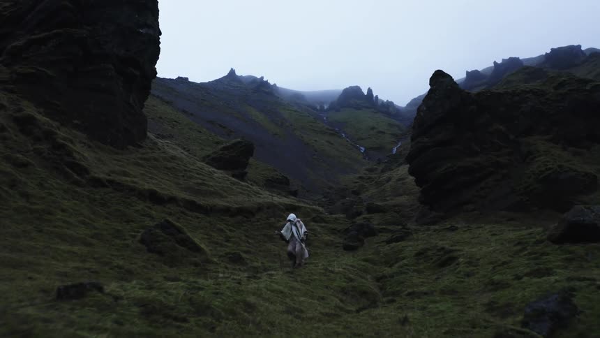 Isolated person with a staff and white clothing walking through a mountain valley