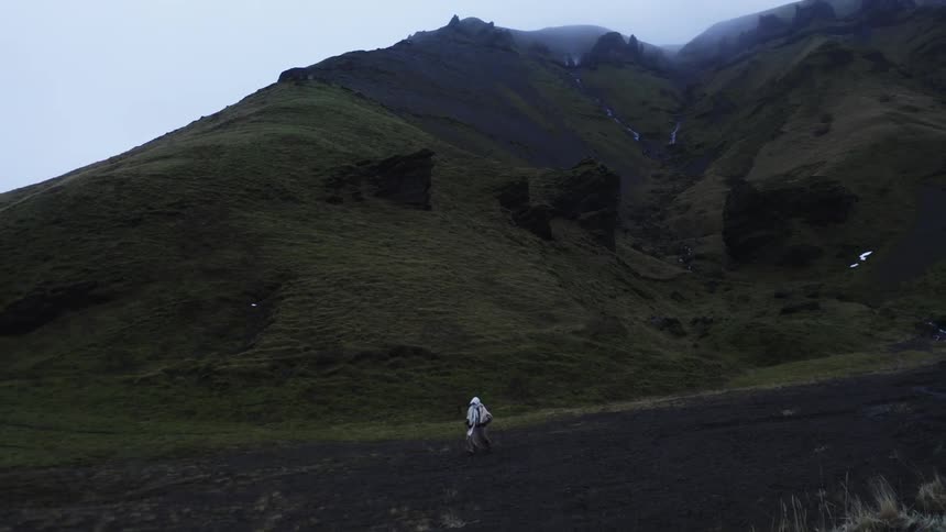 A person dressed all in white walking on a path of dark ground next to a mountain