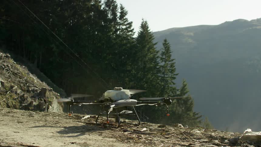 A large spray drone starts its propellers and soon lifts from the ground on-site