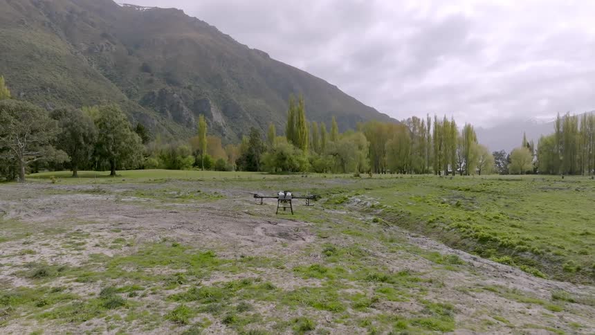 Drone taking off from a field near a lake on a cloudy