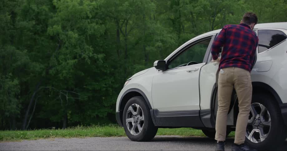 Man stopping his white car and opening the door for his dog and they both run off into a grassy wood