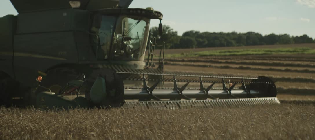 Worker drives agricultural machine across a crop field on a farm on a sunny day