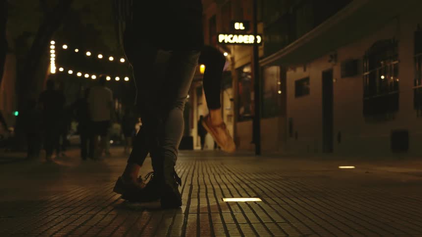 Legs of a man and a woman in a public square at night dancing tango