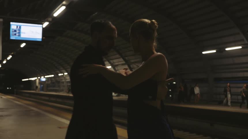 A couple dancing a tango on a subway station while the commuters look on
