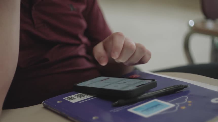 Individual sitting with a textbook and using a smartphone