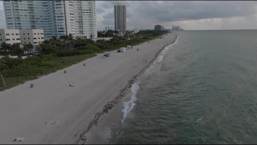 A beach with some waves breaking on the sandy shore with some people walking