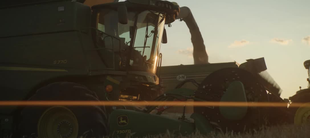 A green john deere combine harvester actively working in a field during sunset