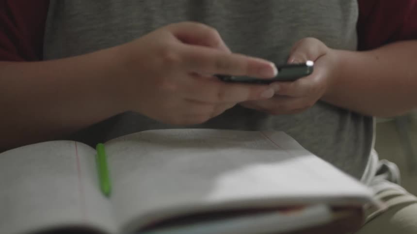 Person sitting holding a pencil on a book and picking up a cell phone and typing