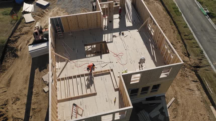 Wooden construction in progress with structural walls erected and planks spread across the floor of a house