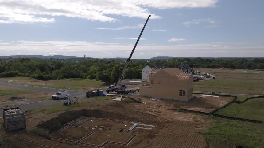 A crane positioned near a partially constructed house on a construction site