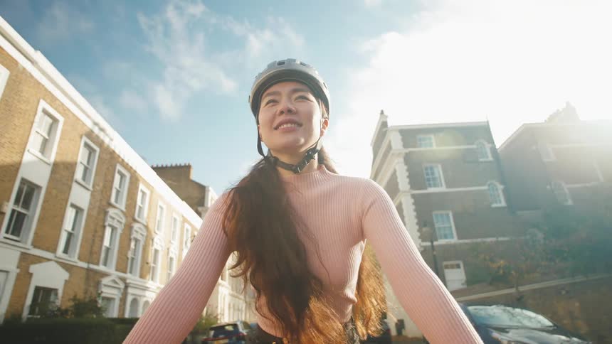 Woman in helmet with happy facial expression riding a bicycle in a city