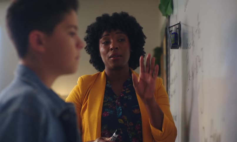 Student standing next to the teacher looking at a whiteboard and focusing on the explanation