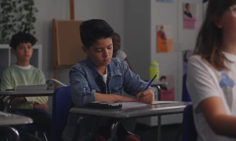 A classroom with students seated at desks writing or taking a test