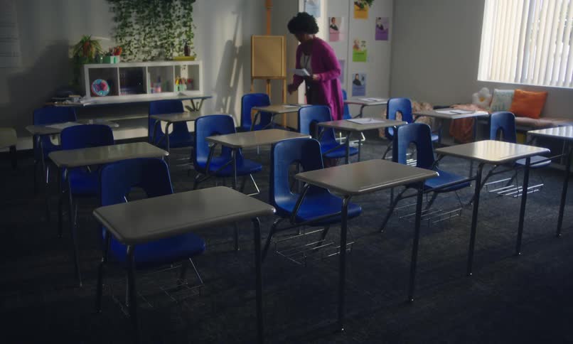 Female school teacher places papers and pencils on desks in an empty classroom while the preparing room for a test