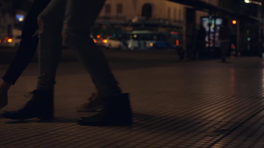 The feet of two people dancing a tango on a city street at night
