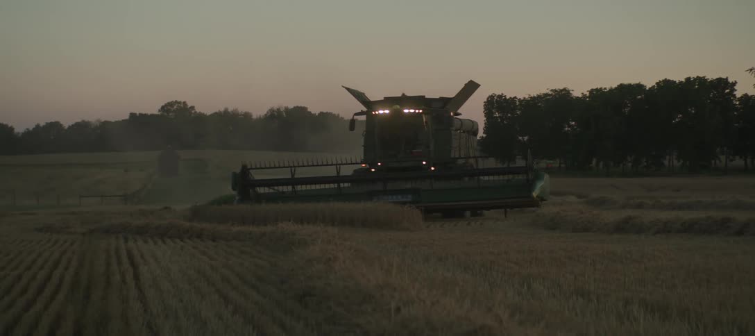 A combine harvester working in a field expelling dust and crop debris from its rear