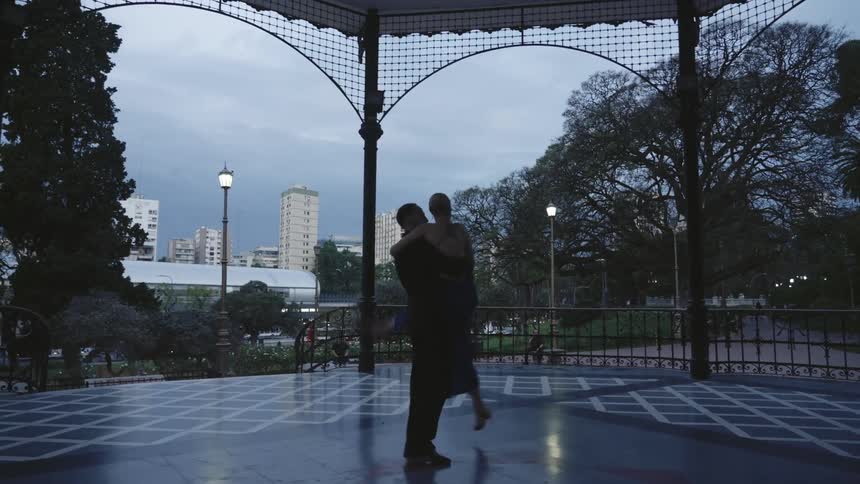 An elegant couple dancing on an outdoor pavilion in the city at dusk