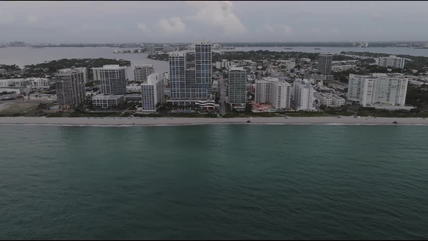 Aerial view of coast line beach lined with tall hotel buildings on an island peninsula next to the ocean