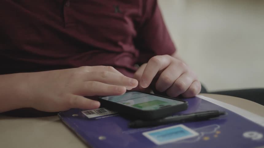 Person typing on a smartphone on the table with a pen next to it