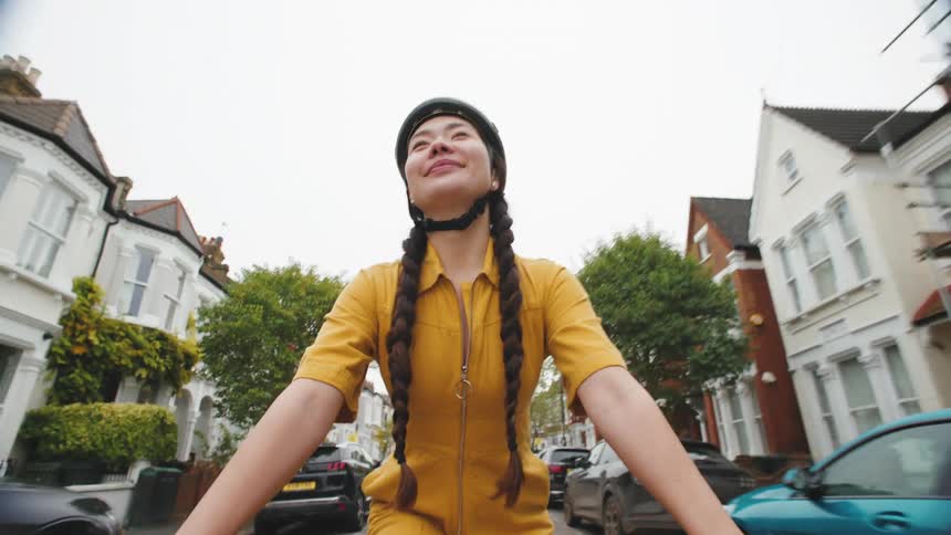 A young asian woman rides a bicycle in a suburb on a cloudy summer day