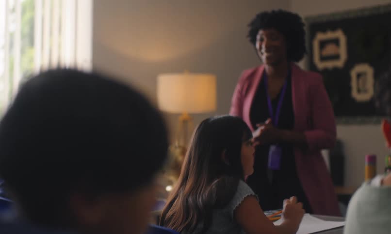 Classroom with a teacher interacting with students and one of them writing