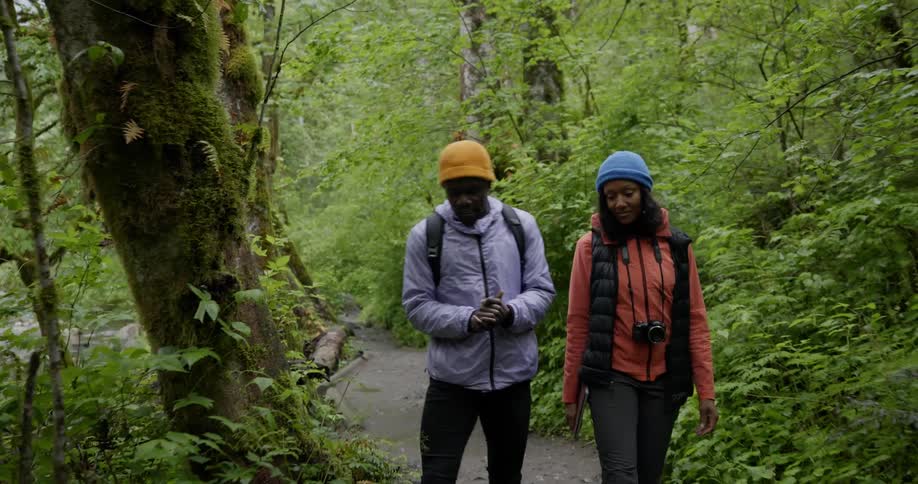 Two people hiking on a trail through the forest alongside a riverbed