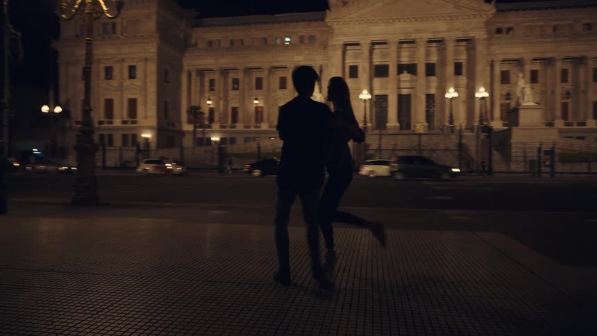 Silhouette of a couple dancing tango on the city streets at night