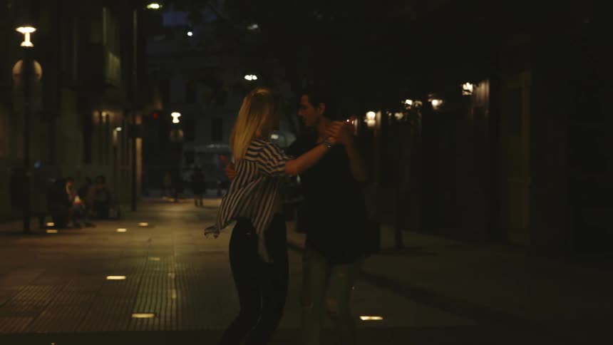 Man and woman dancing down a dimly lit street at night