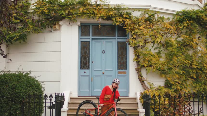 A woman on the phone carries her bicycle down stairs from the front door