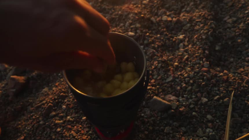 Man stirs food with a wooden spoon while cooking outdoors