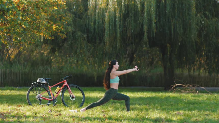 Woman in a park with trees and a lake in the background doing yoga positions