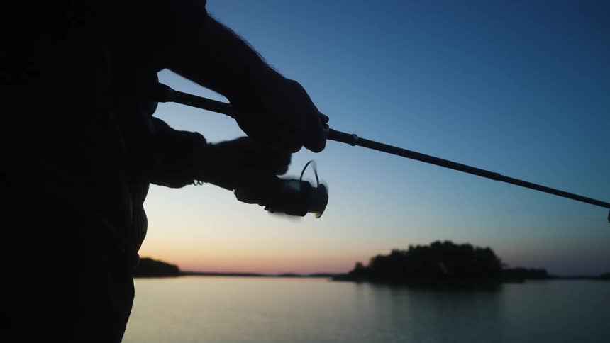 Silhouette on the arm of a person pulling the line of a fishing rod next to a lake