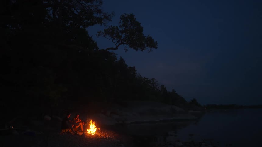 Couple sitting next to a campfire in a cove on a sandy beach at night