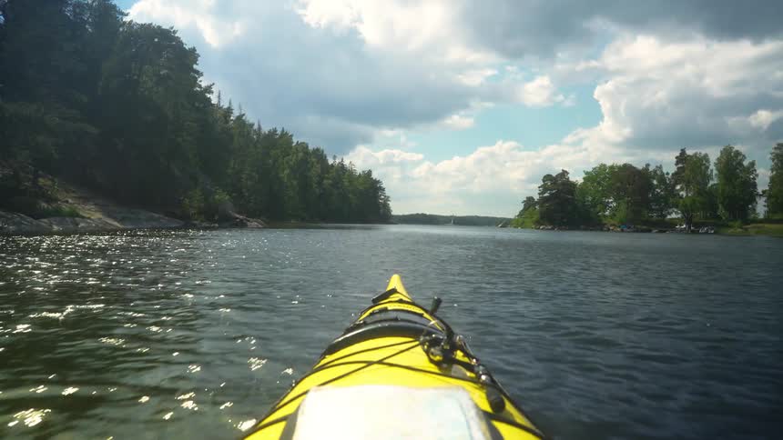 A yellow kayak moves down a river bordered by forests