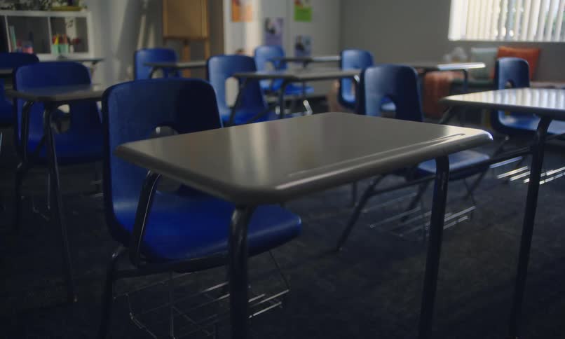 An empty classroom with rows of blue chairs and tables
