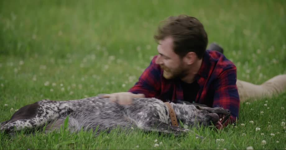 Man lying on the grass with his dog petting his body