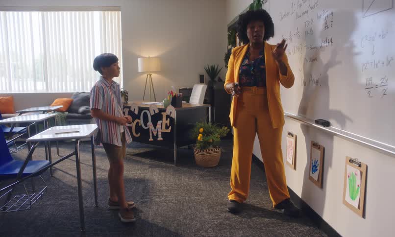 A teacher writes an algebraic equation on the board for one student standing in a classroom