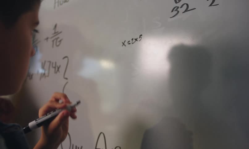 A teacher watching a student solving math problems on a whiteboard in the classroom