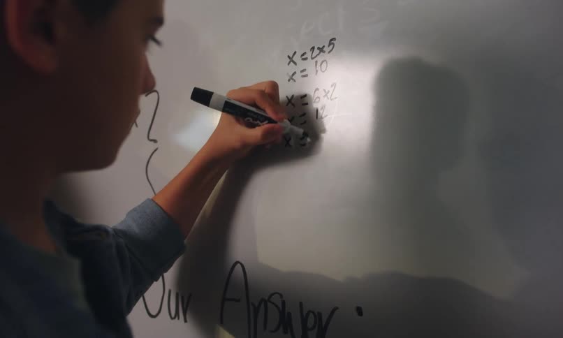 Teacher gives student a pat on the back for solving a math problem on the white board