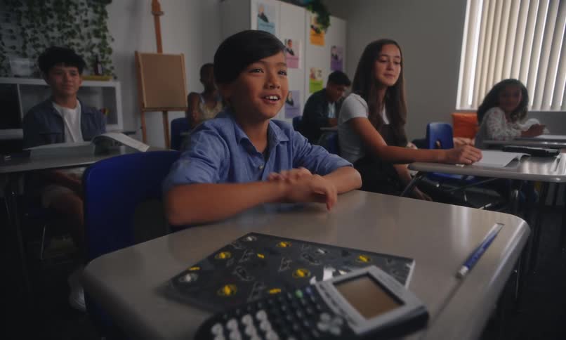 Students sitting in a classroom with one of them raising his hand