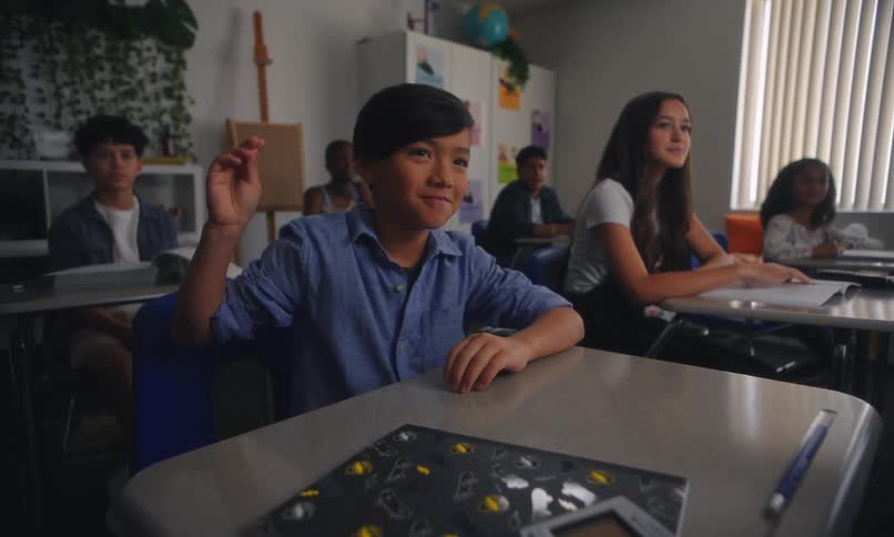 A student sitting in a classroom raises his hand