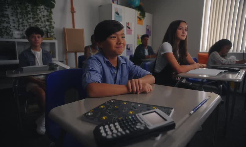 Smiling boy in classroom next to his classmates raising hands