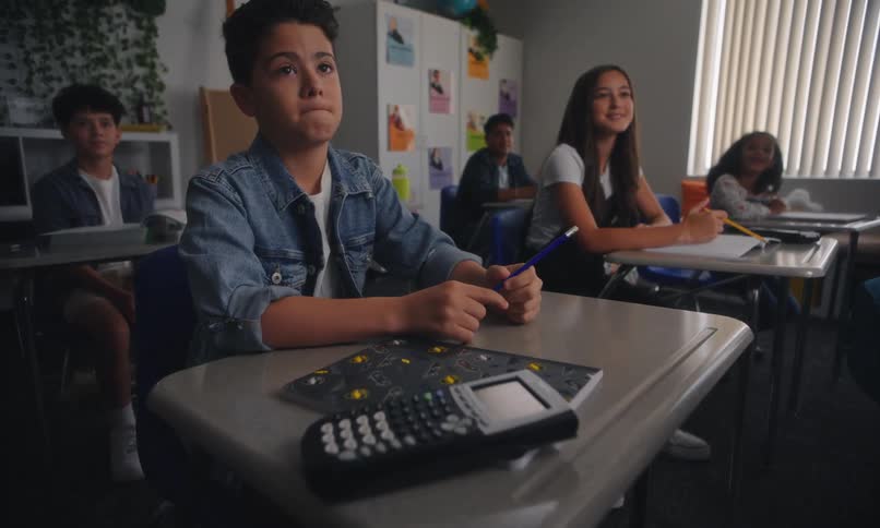 Boy sitting in the classroom and answering a question and then changing expression to confused with other students around