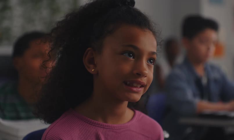 A girl sitting in a classroom listening to a teacher giving class