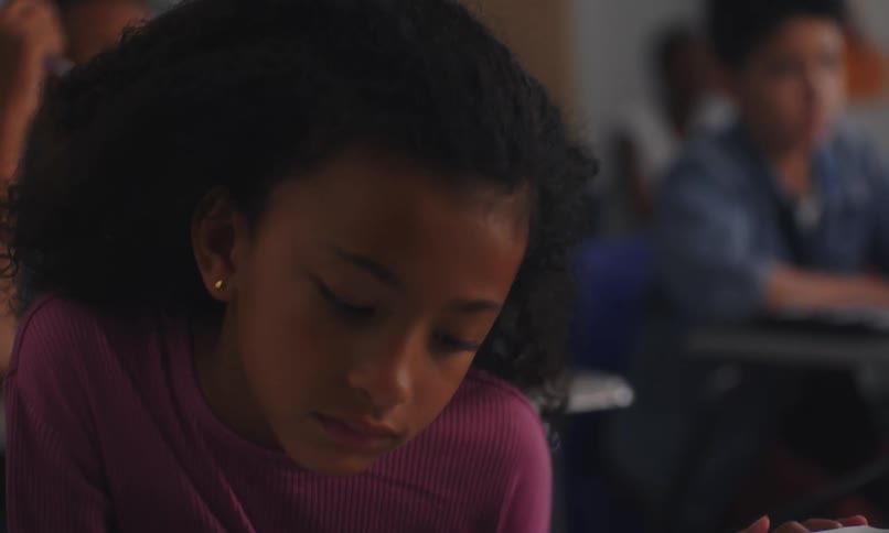 Portrait of a little girl sitting in the classroom holding a beautiful pencil and other students in the background